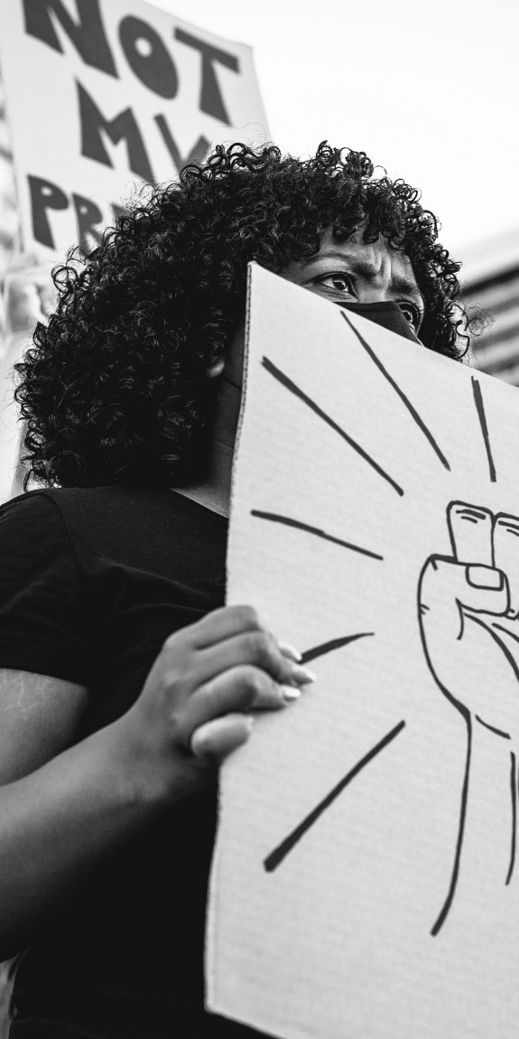 Black woman at a protest holding a sign with a raised fist painted on it