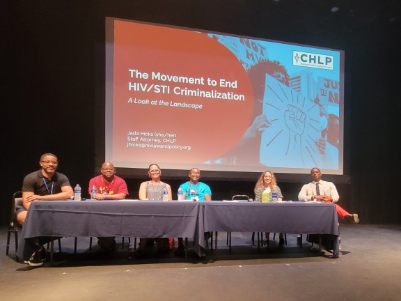 Six panelists sitting in front of a large screen