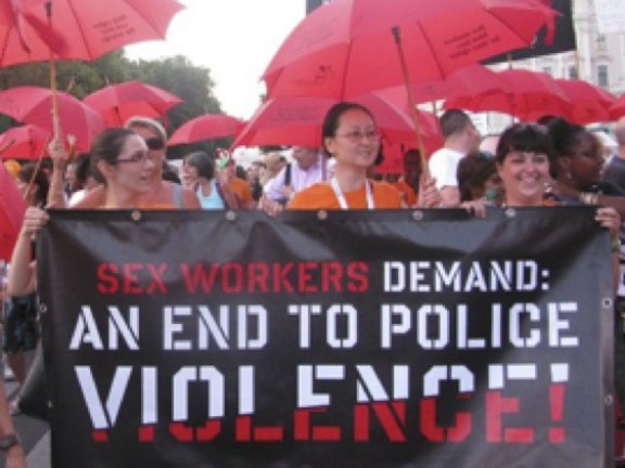 Women with Red Umbrellas marching with Banner Reading Sex Workers Demand and End to Police Violence