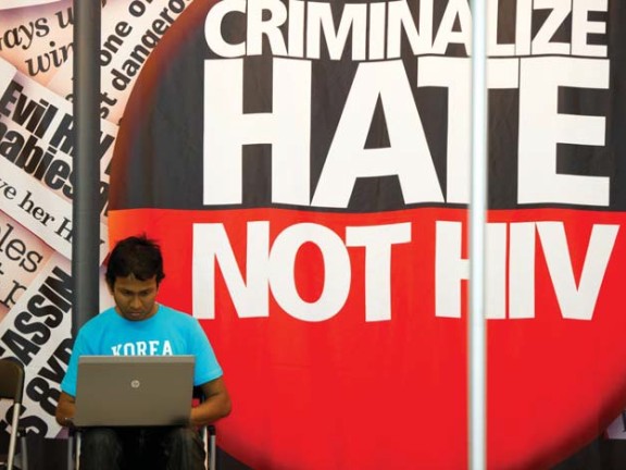 Speaker in front of Criminalize Hate not HIV banner.