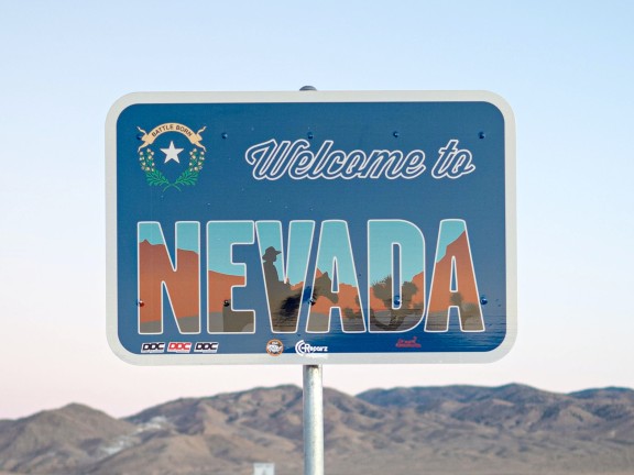 Sign reading Welcome to Nevada with mountains and blue sky behind.