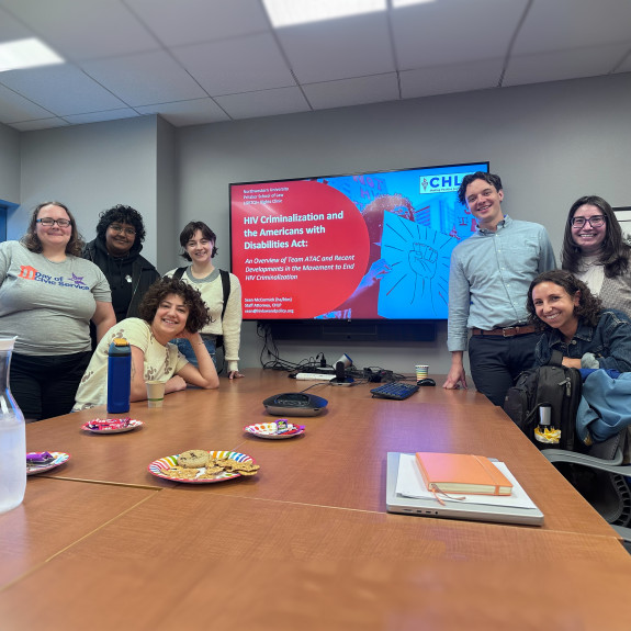 A group of people standing around a conference room table smiling at the camera.