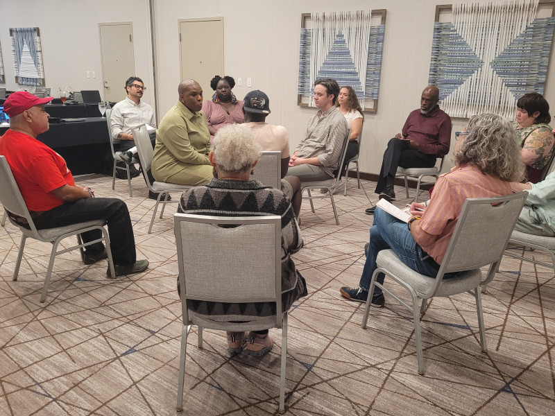 Twelve people sitting in a circle on being metal chairs in a beige conference room.