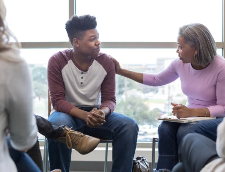 Young black man being counseled by an older black woman with her hand on his shoulder.