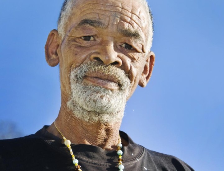 Black elder in black tee looks at camera with blue sky behind him.