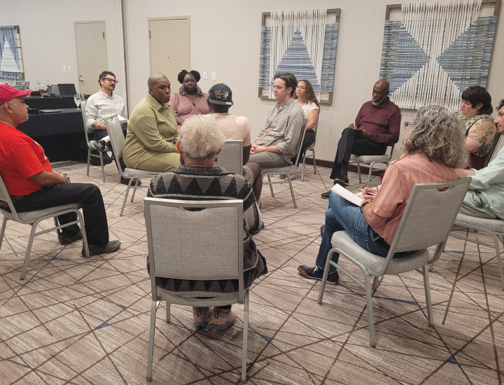 Twelve people sitting in a circle on being metal chairs in a beige conference room.