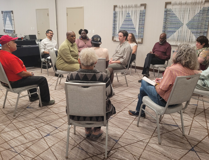 Twelve people sitting in a circle on being metal chairs in a beige conference room.