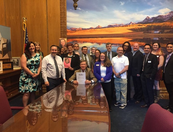 Group of 15 people standing around governor at a big desk for bill signing