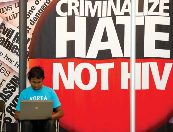 Speaker in front of Criminalize Hate not HIV banner.