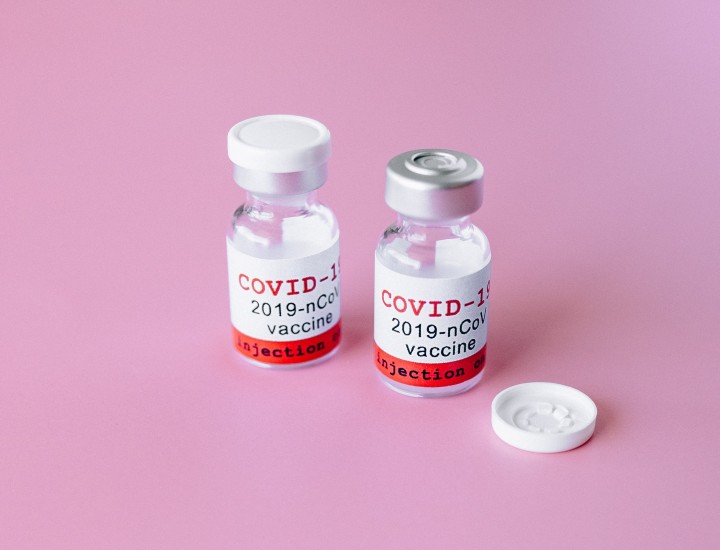 Two covid vaccine bottles against pink background